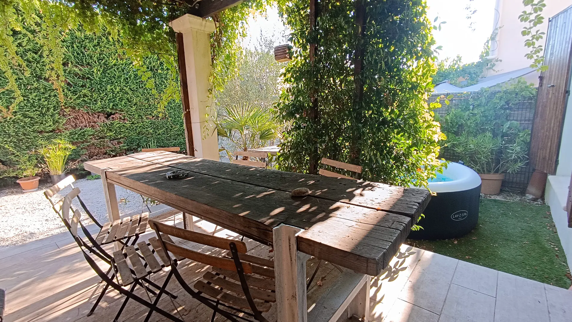Terrasse ombragée avec pergola végétalisée et grande table familiale en bois pour les repas en extérieur.
