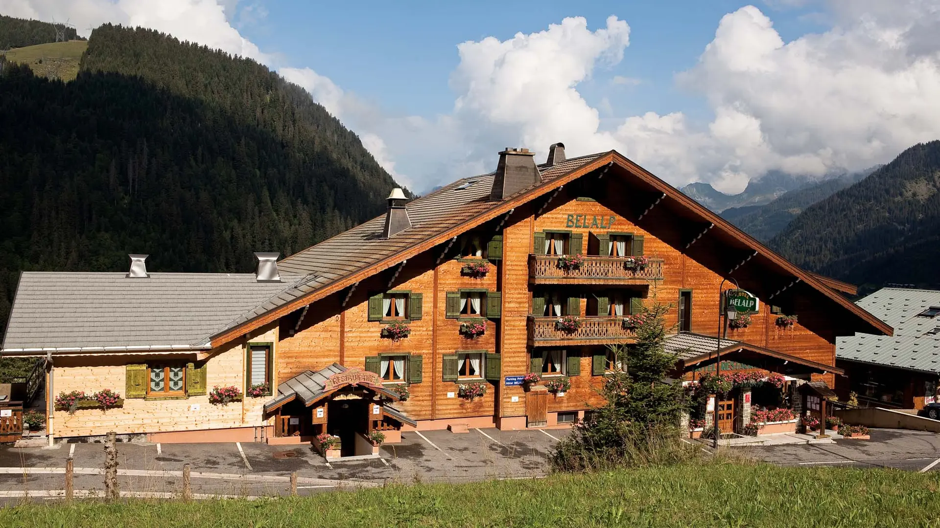 Façade de l'hôtel en été, avec les fleurs aux balcons et les montagnes en arrière plan
