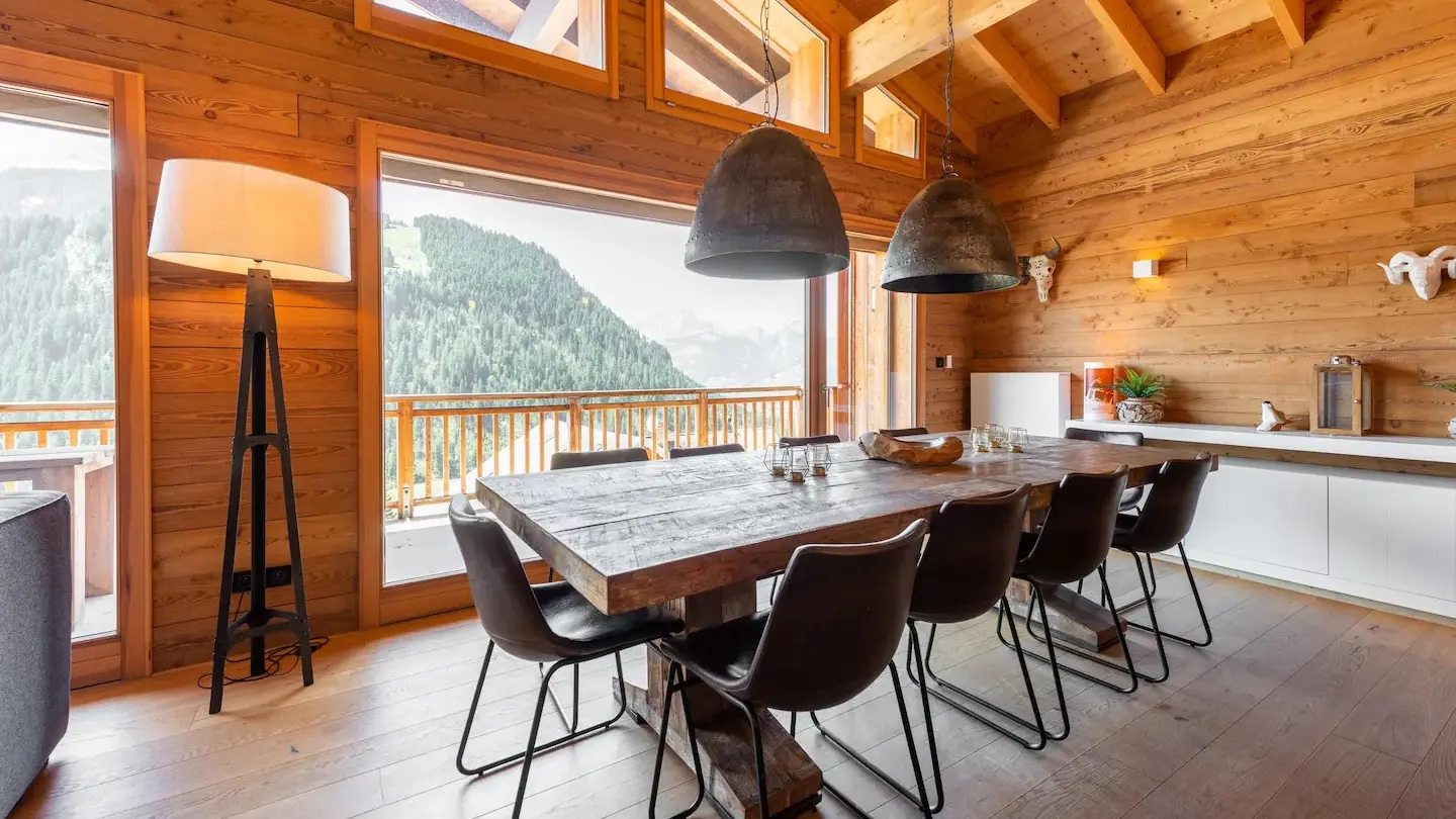 Salle à manger avec une grande table, grandes baies vitrées offrant une vue panoramique sur les montagnes