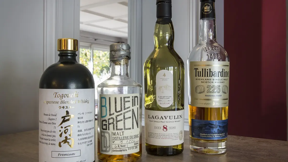 4 bouteilles de différents whisky posés sur un bar en bois.