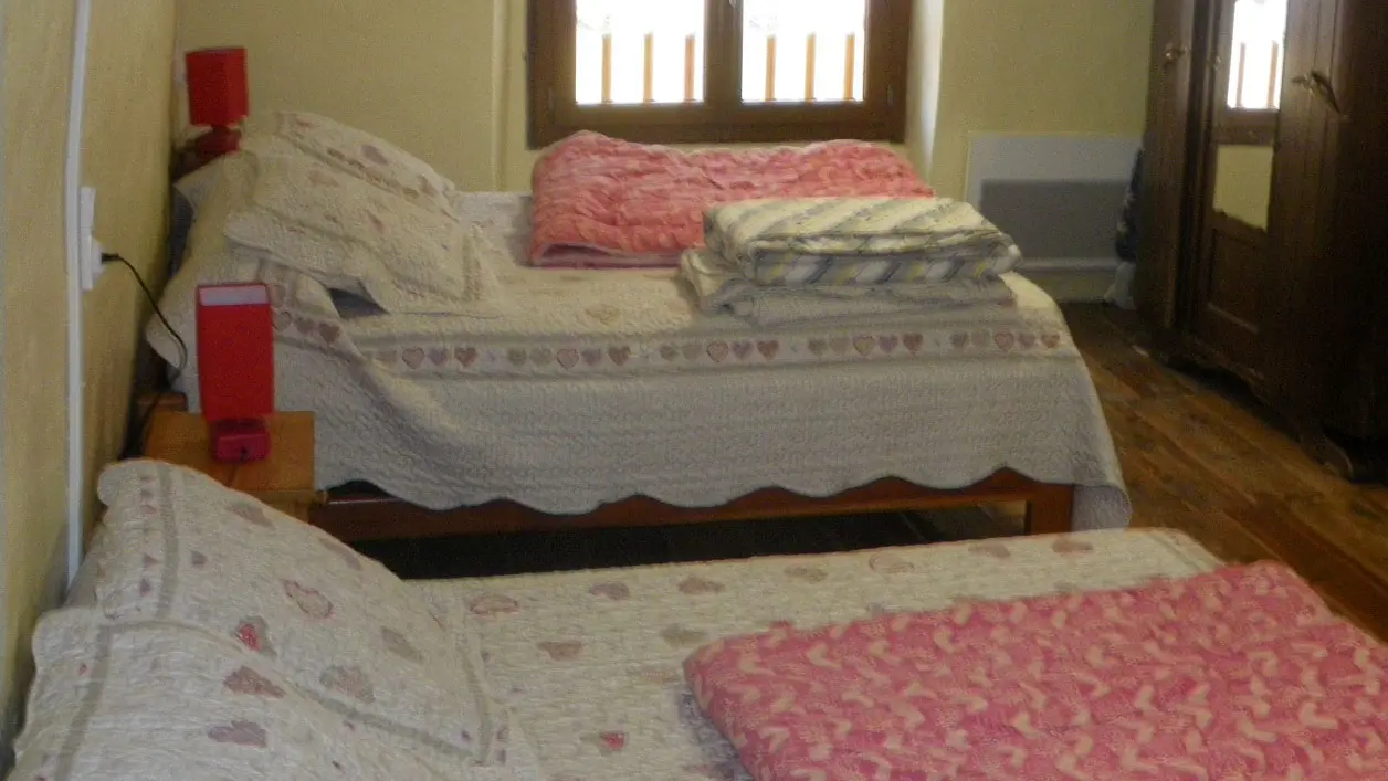 Chambre à coucher lumineuse avec deux lits doubles, ameublement bois, parquet au sol, fenêtre