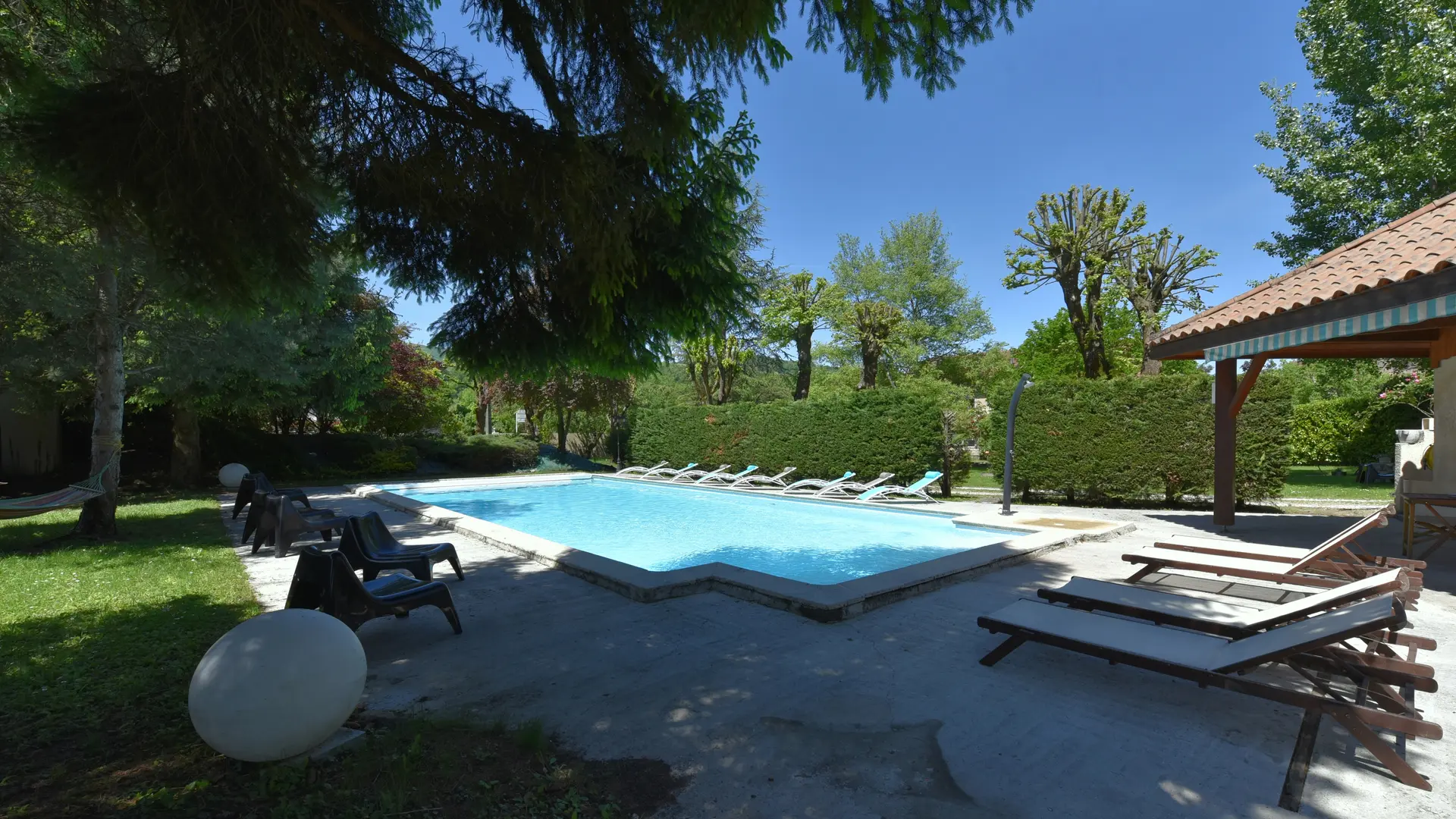 Grande piscine extérieure bordée de sièges et de transats, au cœur d’un cadre verdoyant