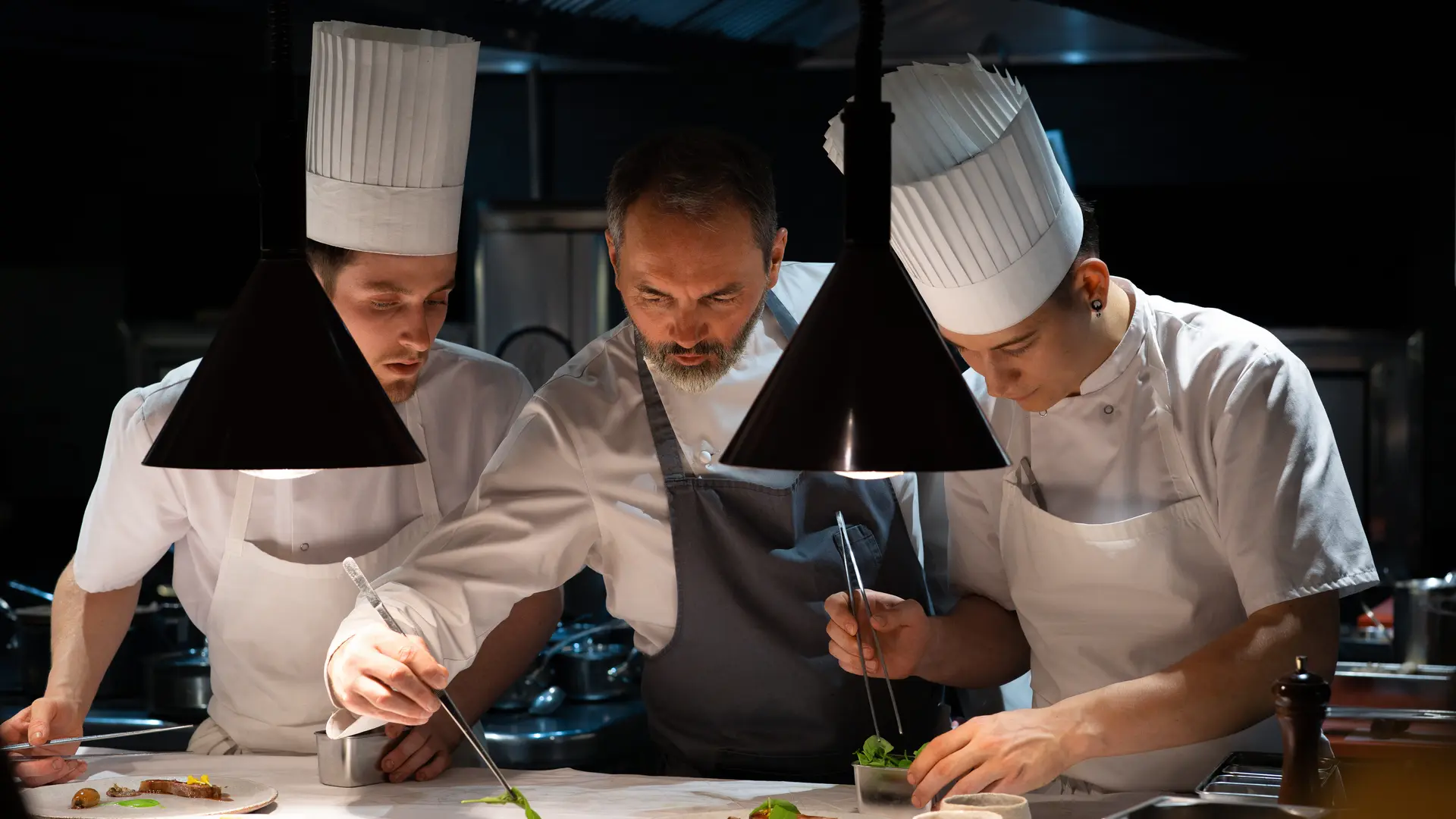 Christophe Aribert préparant un plat entouré de deux cuisiniers