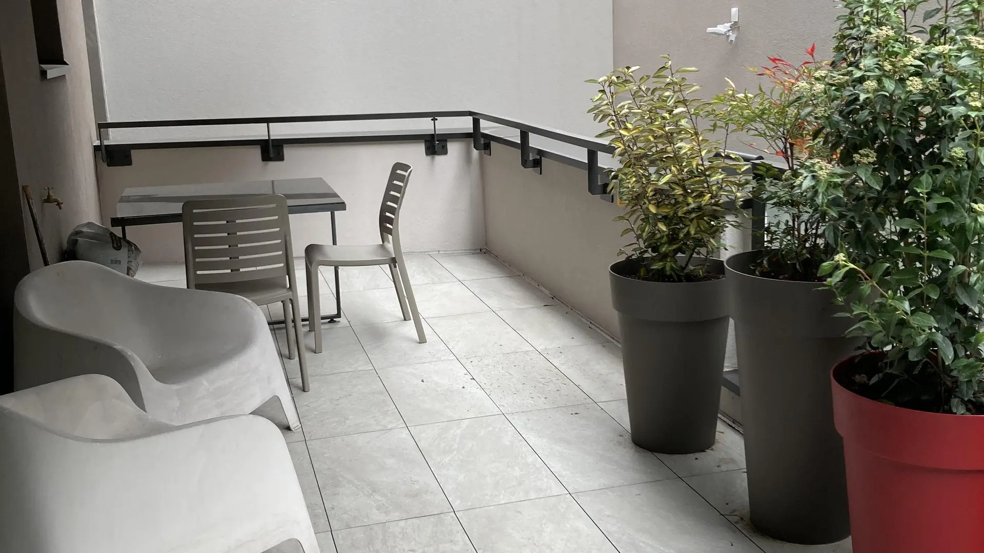 Vue de la terrasse avec le mobilier de jardin gris et 3 buissons dans de grands pots