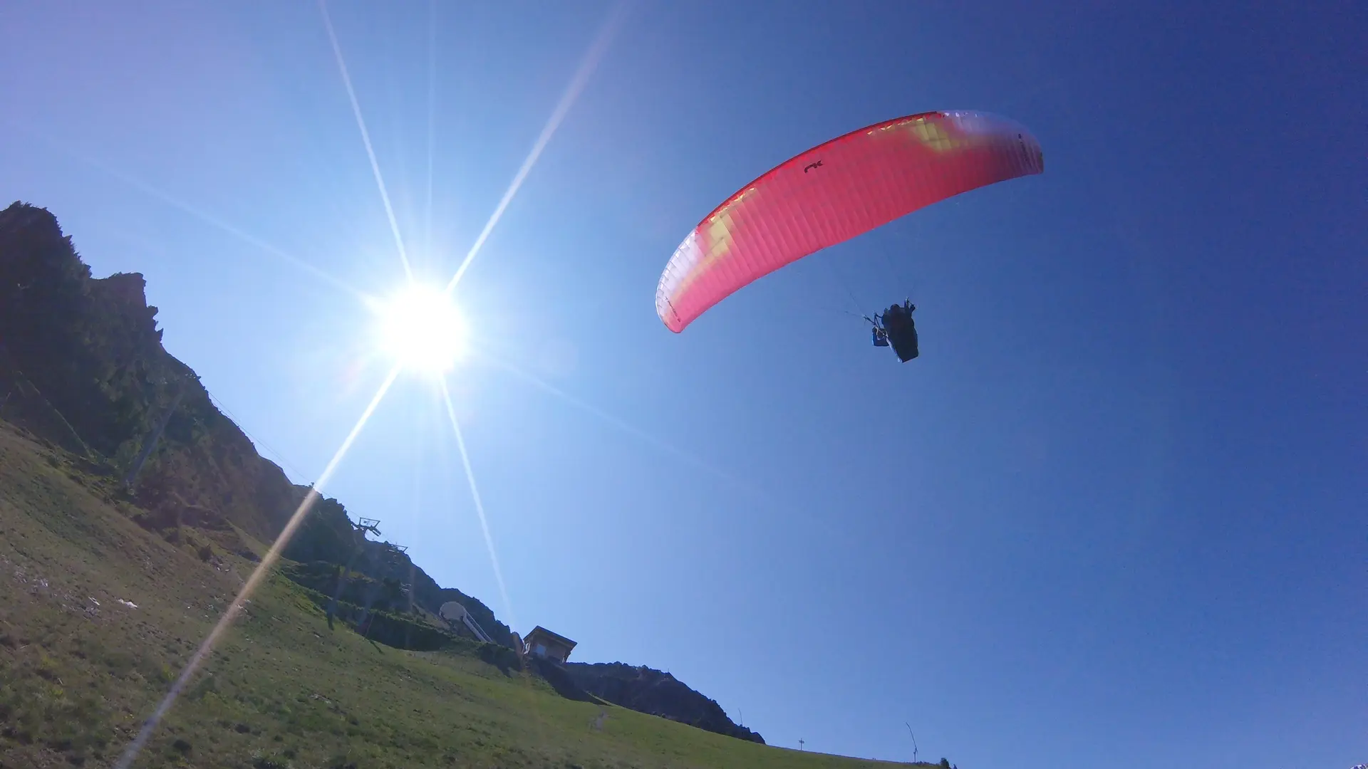Vue depuis le sol, parapentiste avec une voile rouge sous un ciel bleu dégagé