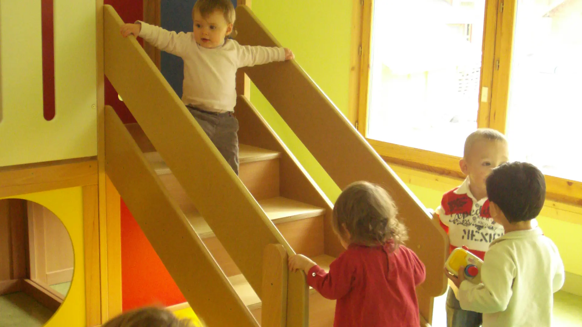 5 enfants jouant autour d'une structure de la salle de jeux, l'un d'entre eux debout sur les escaliers en bois de cette structure