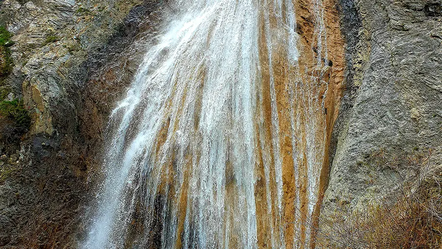 Cascade de Chaumie, cascade rocheuse se déversant depuis une forêt de conifères dans un petit bassin naturel creusé dans la roche