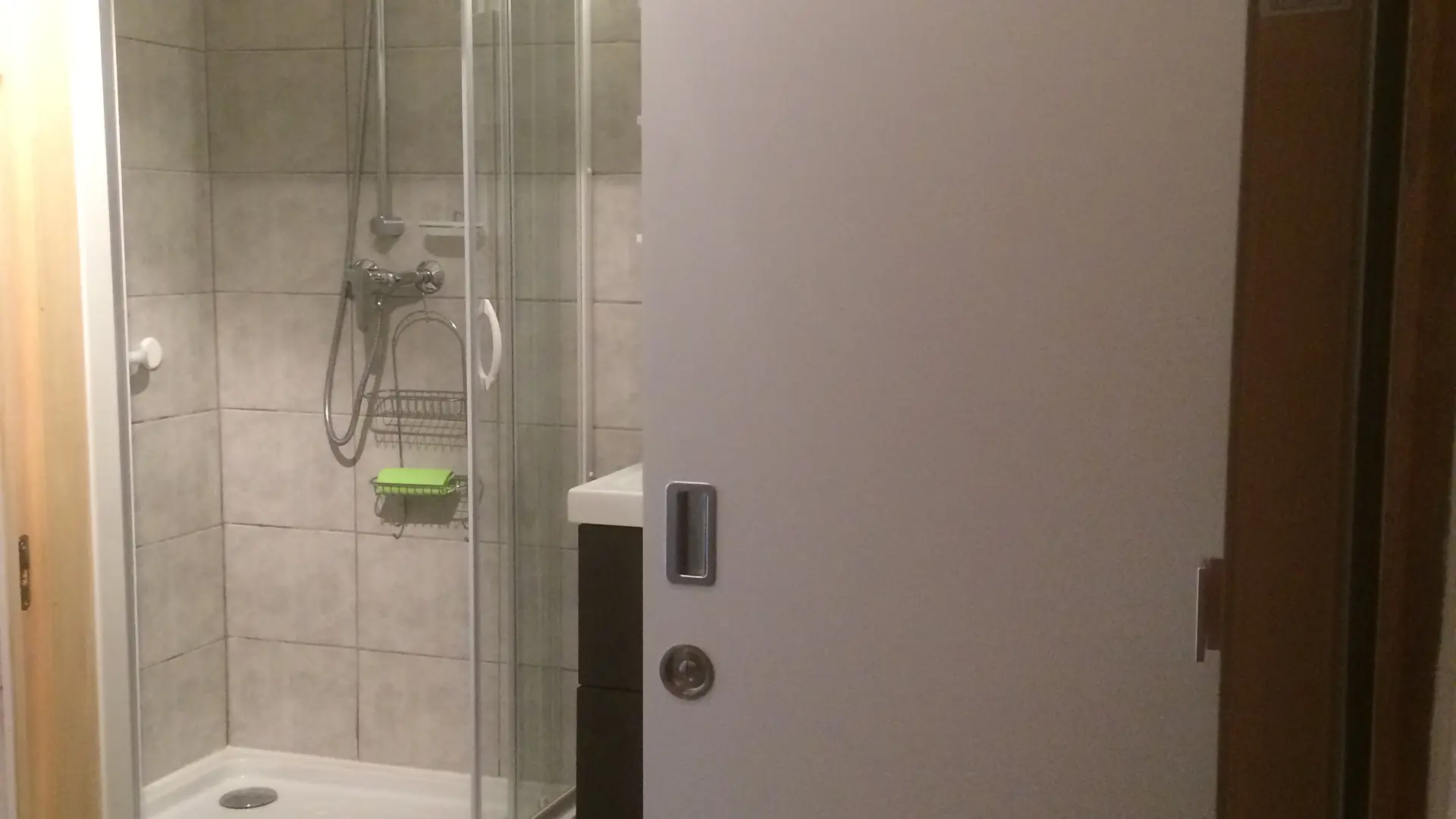 Une salle d’eau, la porte de la douche est ouverte, révélant une cabine de douche arrondie avec des parois en verre.