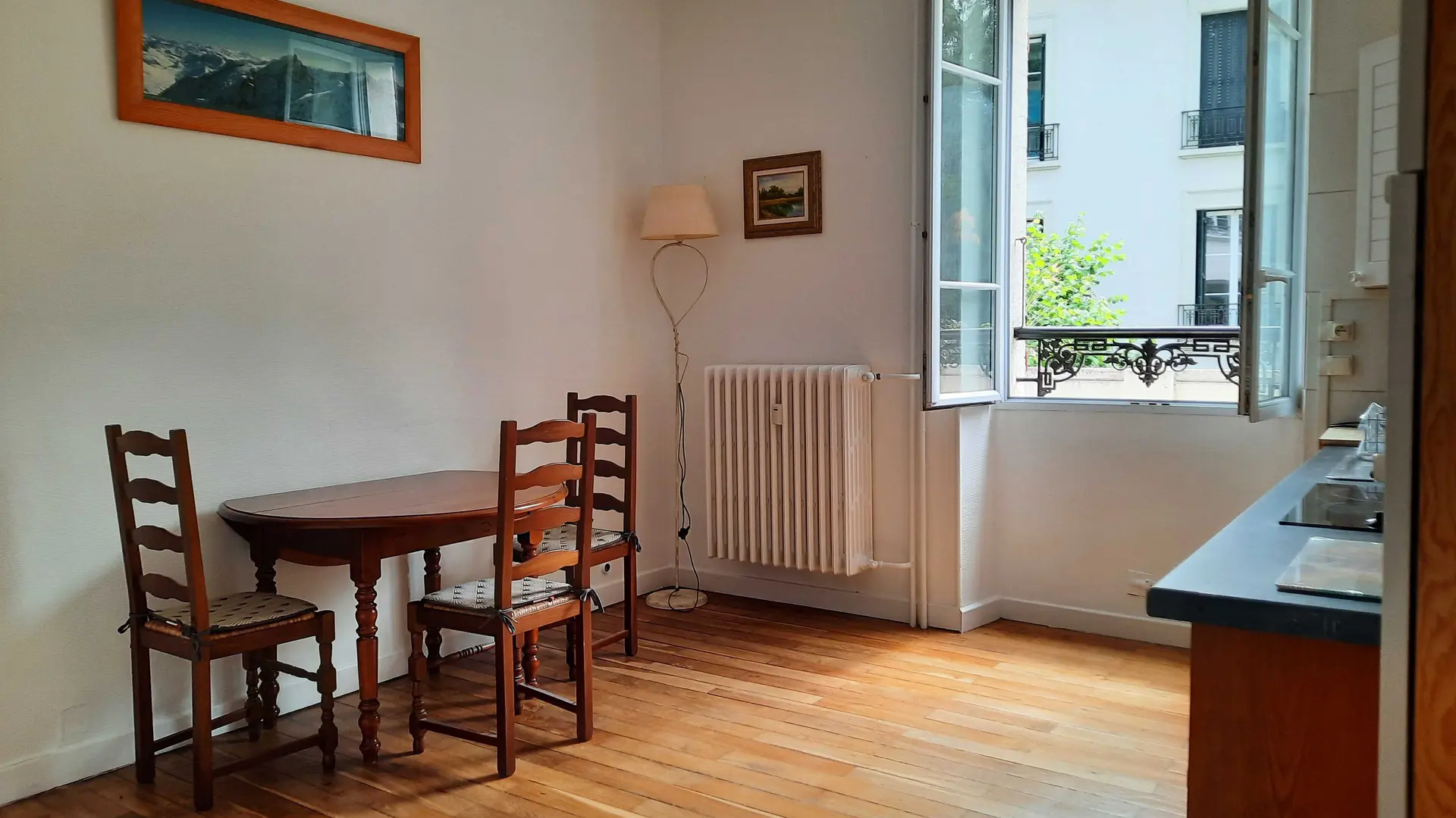 Cette pièce est meublée d'une table ronde en bois avec trois chaises, d'un meuble de rangement bas sur la droite, et de tableaux aux murs.
