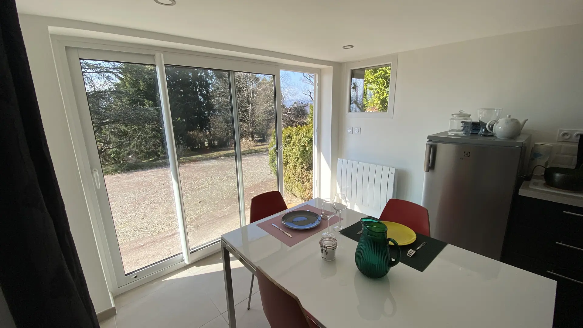 Le studio est lumineux et donne sur un jardin par une grande baie vitrée. Il est équipé d'une cuisine ouverte sur la pièce principale, où se trouve une table de salle à manger entourée de quatre chaises.