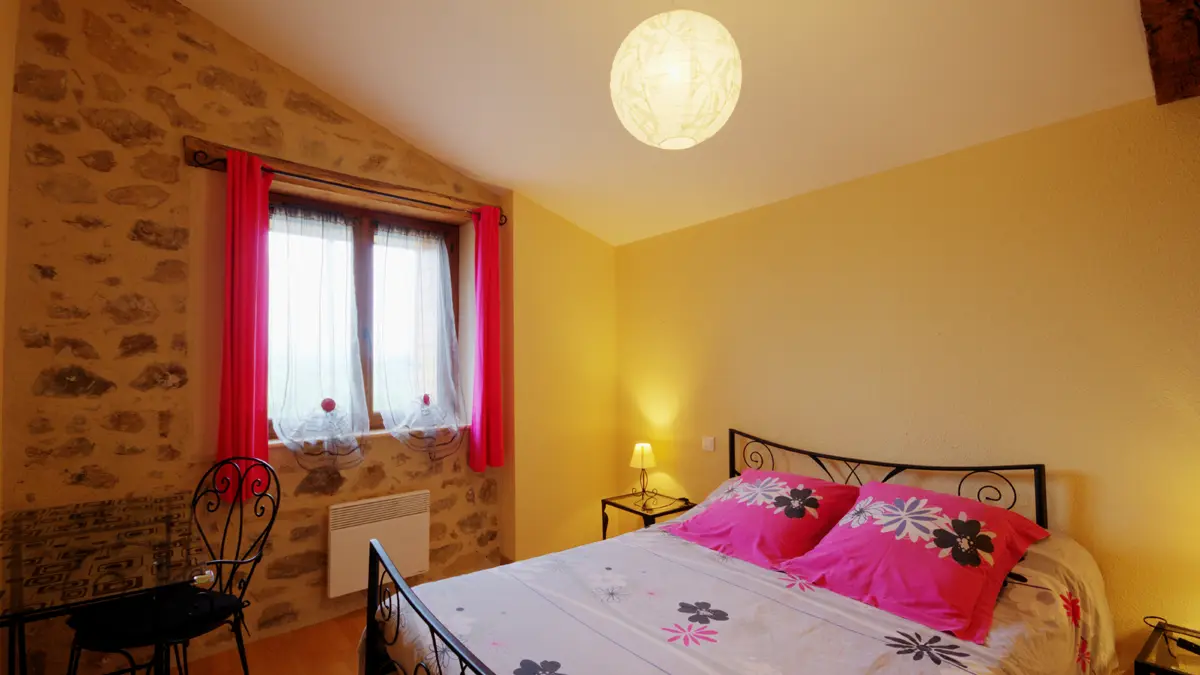 Chambre fushia et gris à l'étage avec un lit en 140 et table en verre servant de bureau.