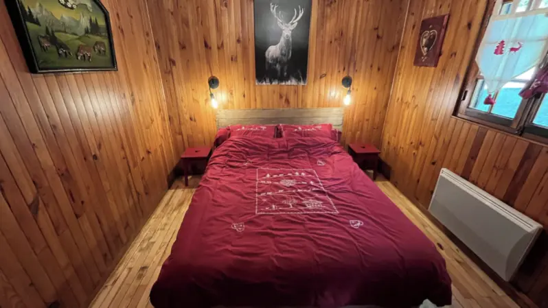 Bedroom with a double bed, wooden interior. Wall-mounted radiator and window with a mountain view.