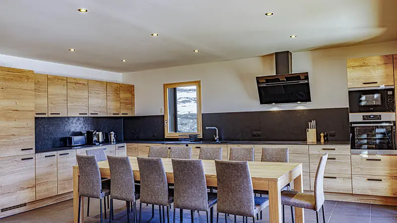 Grande cuisine lumineuse et moderne avec table à manger, TV, fenêtre, ameublement bois et sol carrelé