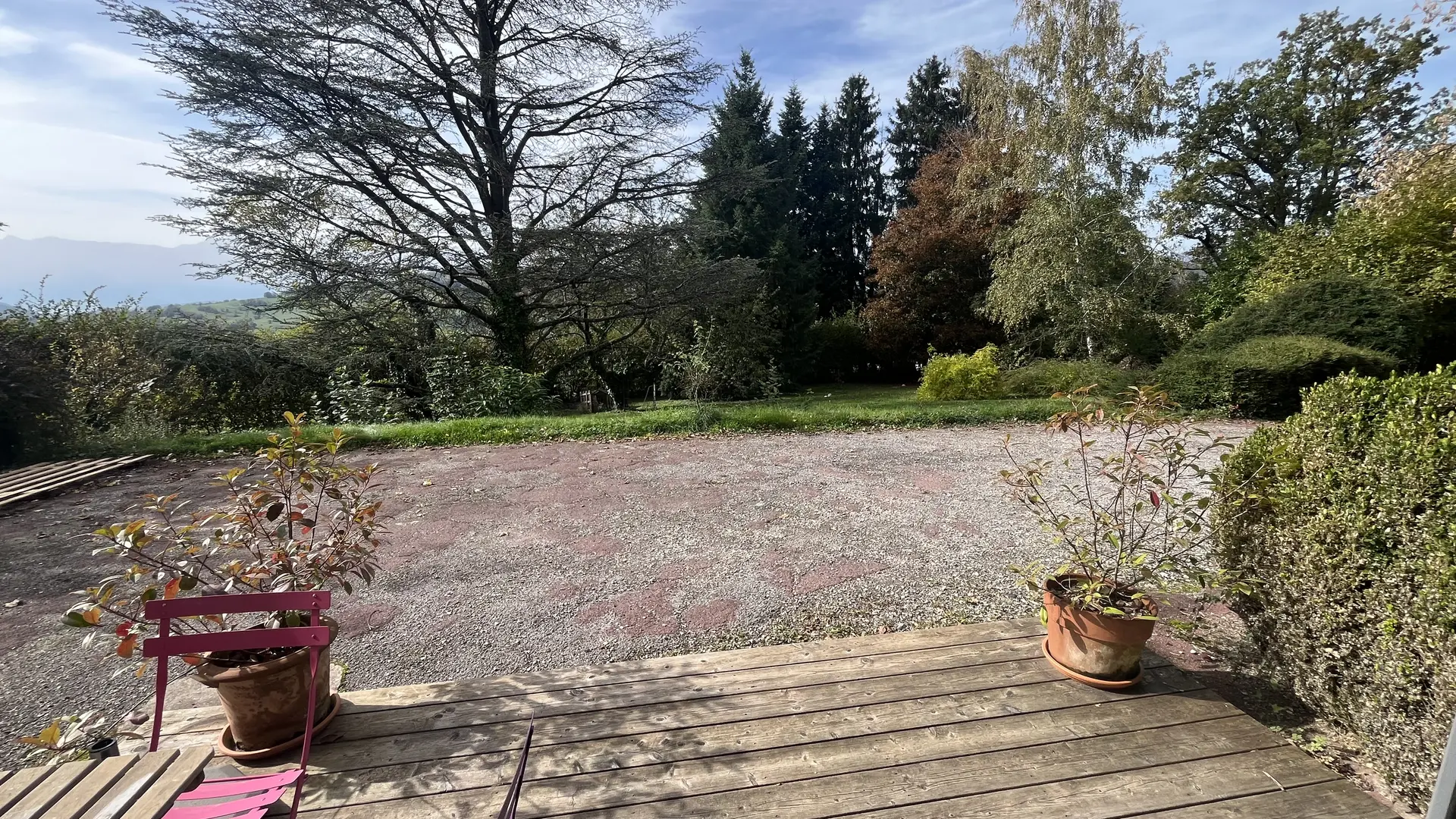 De la fenêtre, vous pouvez apercevoir une terrasse en bois donnant sur un jardin. Des arbres et des arbustes entourent l'espace, créant un coin extérieur verdoyant.