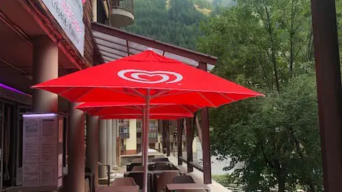 The restaurant's outdoor terrace, in a paved courtyard, with tables and chairs under red parasols.