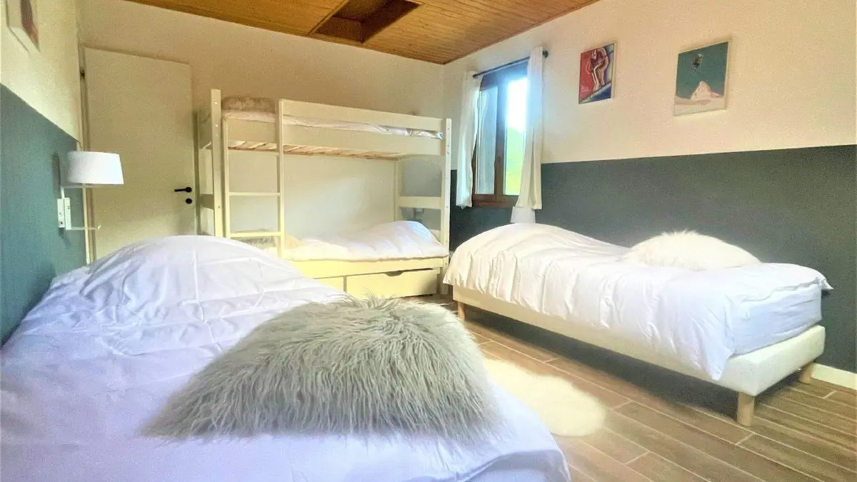 Chambre à coucher lumineuse avec lits superposés et deux lits simples, ameublement bois, parquet au sol, fenêtre