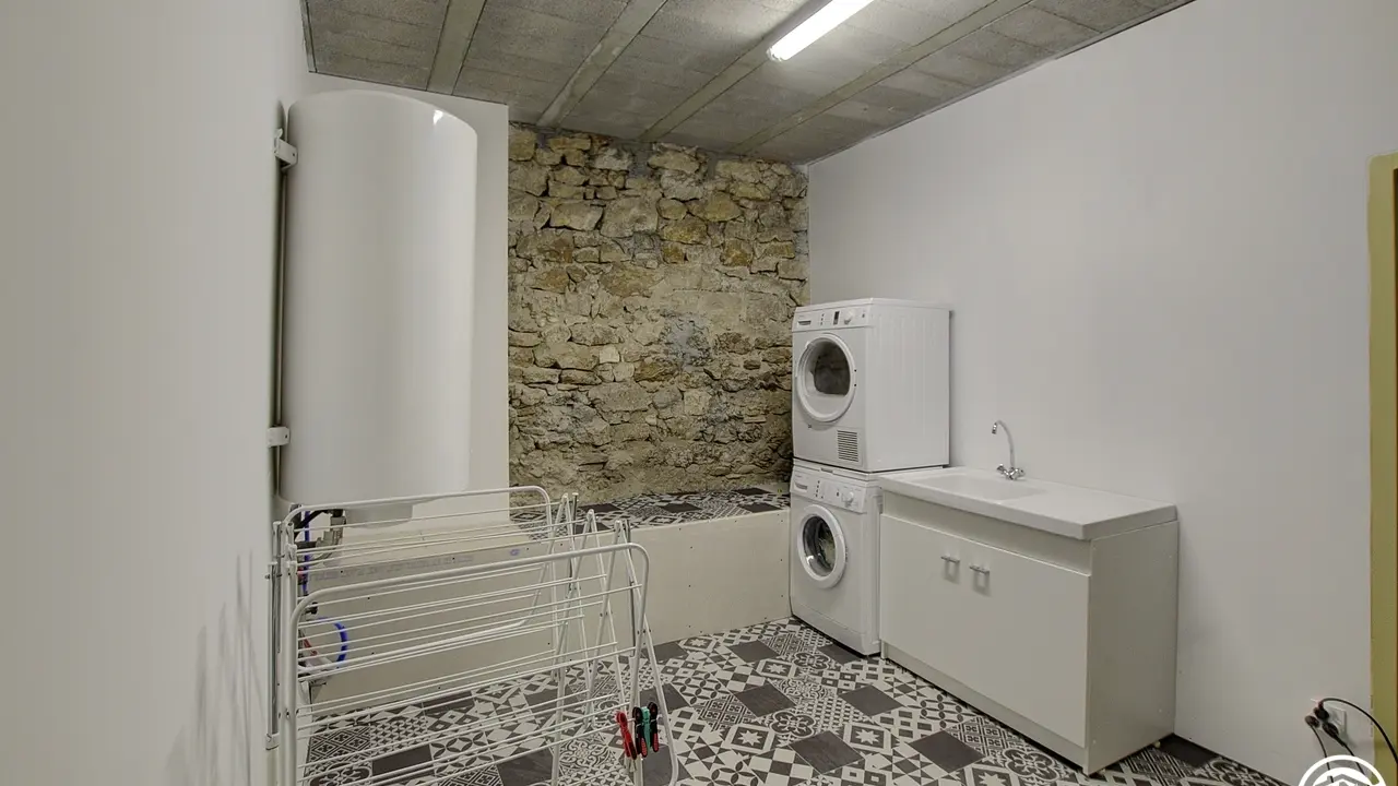Une grande buanderie avec lave-linge  sèche-linge table à repasser et un point eau