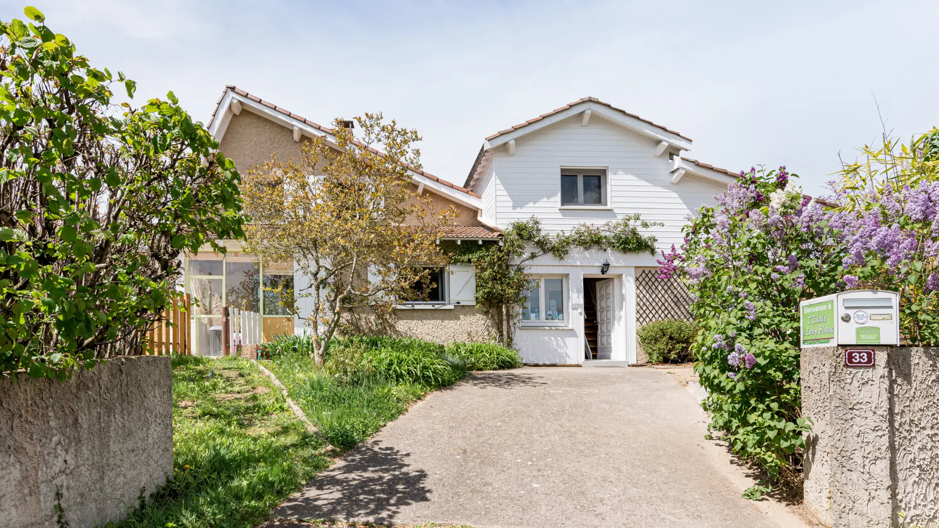 Vue de l'arrivée à L'Escale du Loup Blanc, boîte aux lettres, lilas en fleurs, entrée de la chambre Goélette avec porte ouverte.