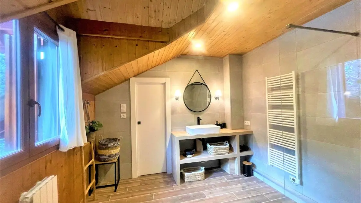 Salle de bains lumineuse avec grand bac à douche, ameublement bois, radiateur, parquet au sol, fenêtre
