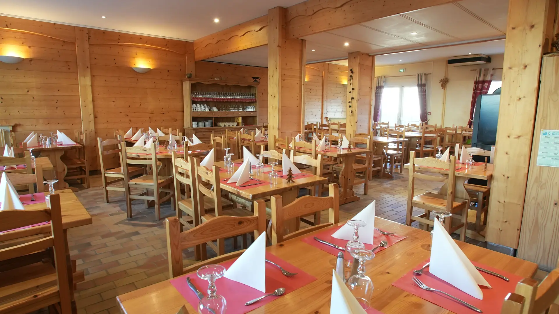 Tables dressées dans un cadre entièrement en bois, éclairage assuré par des appliques murales et des luminaires encastrés au plafond. Les tables sont numérotées avec de petits sapins en bois avec la table n°3 au premier plan