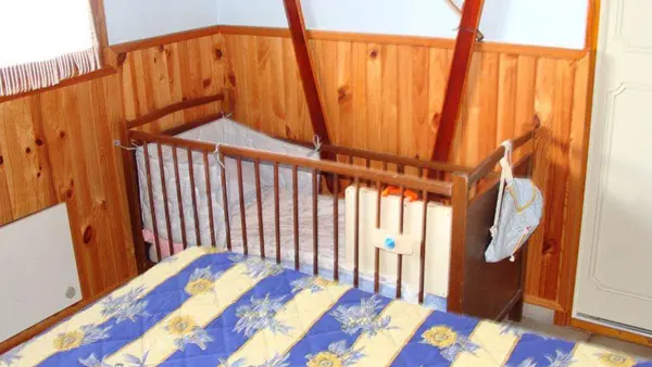 Chambre d'enfants lumineuse avec ameublement en bois et lambris, vue sur lit simple et lit à barreaux pour bébé, fenêtre et rideaux
