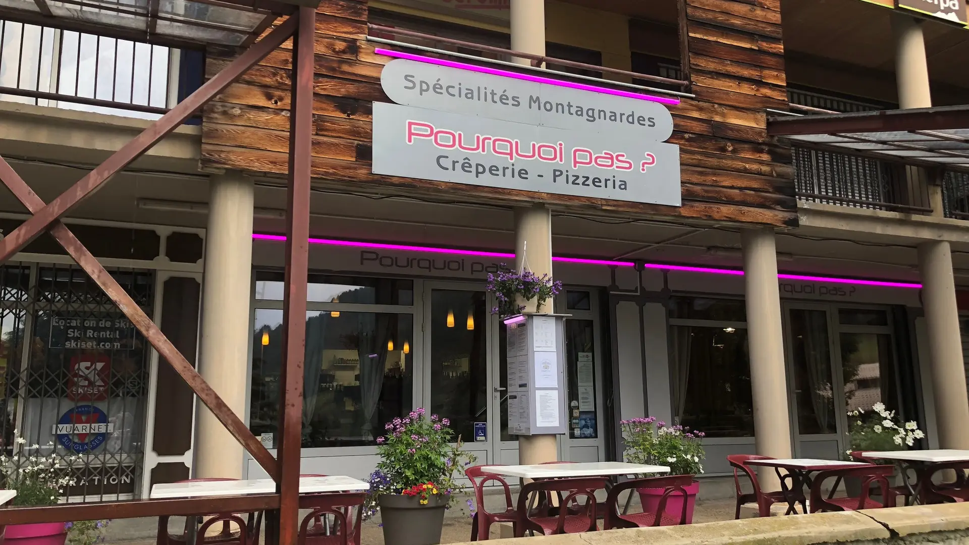Restaurant front with outdoor terrace furnished with tables and chairs. Sign with the inscription : Pourquoi pas ? Creperie Pizza Mountain specialties