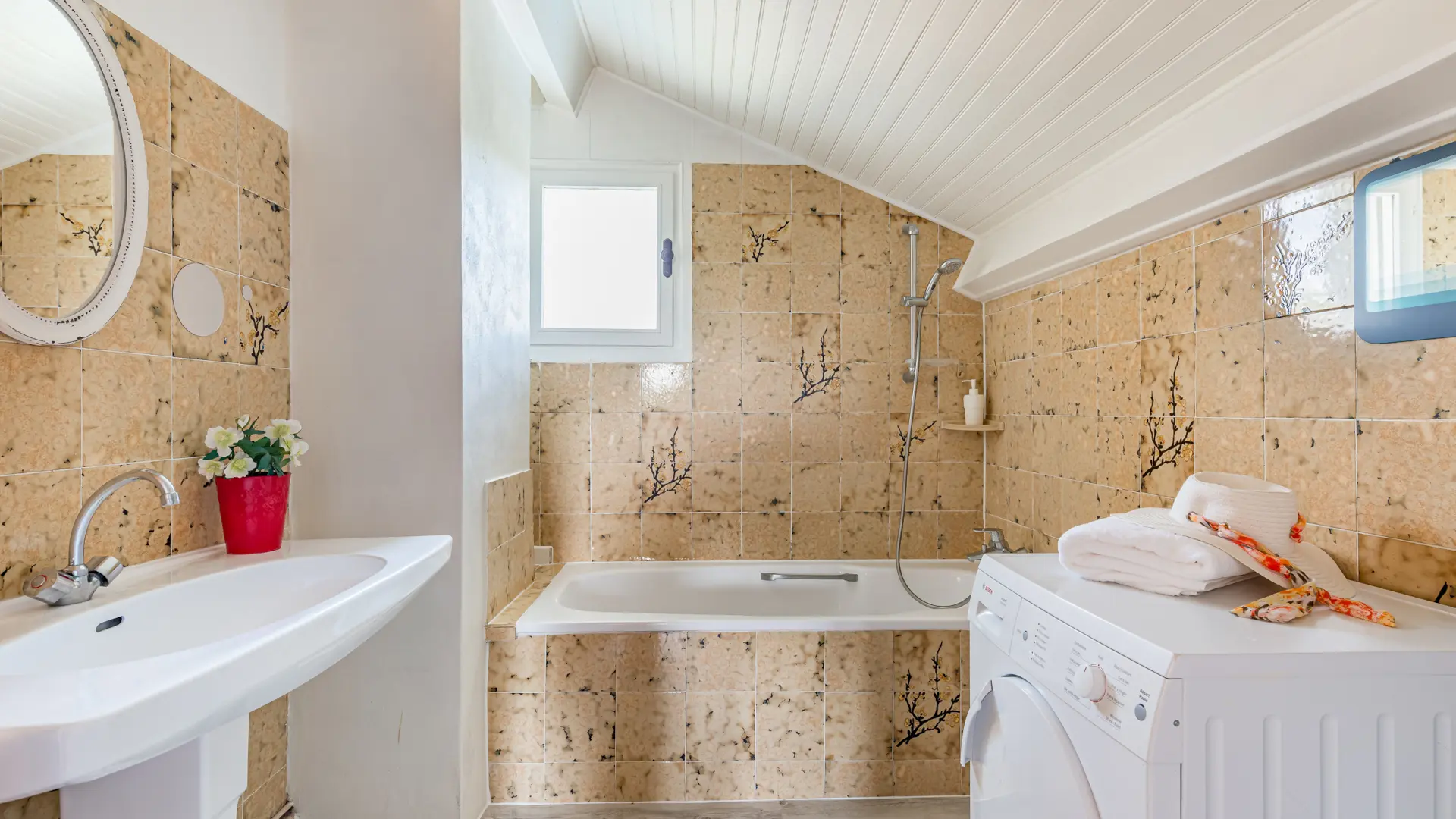 Salle de bain de la suite Perle : baignoire, vasque, chapeau posé sur le sèche-linge et plafond blanc