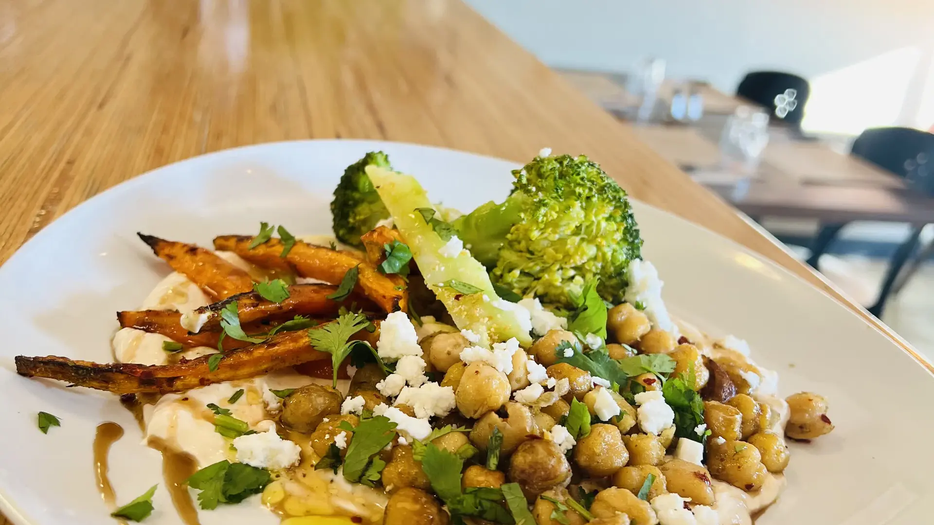 Assiette colorée de pois chiches rôtis, brocolis et carottes grillées sur une sauce crémeuse et herbes fraîches.