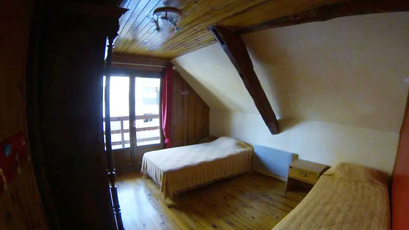 Attic bedroom with two single beds, window, wooden furniture, parquet flooring