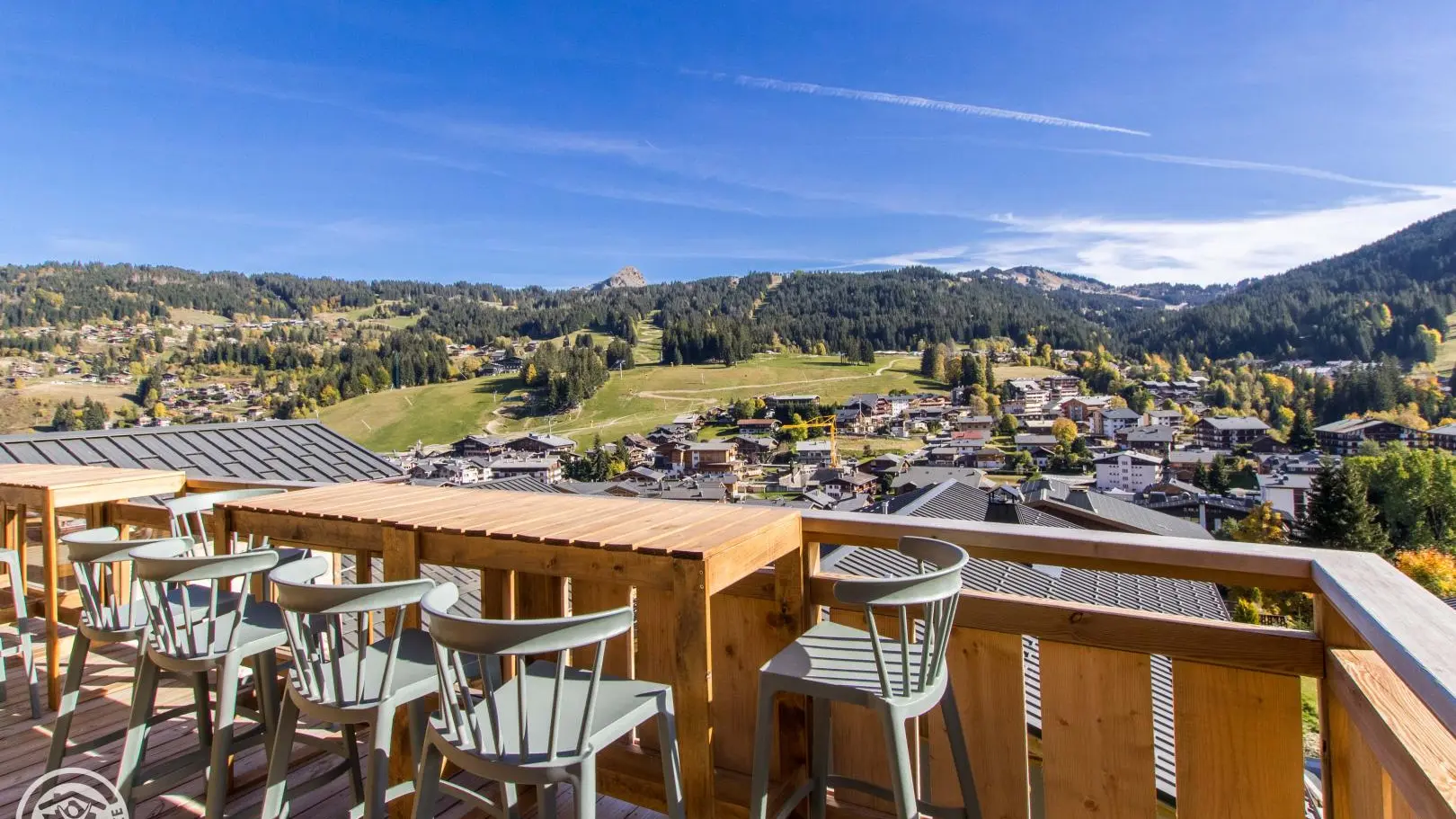 Terrasse de façade, niveau séjour, tables hautes et tabourets, vue panoramique sur le village et les pistes.