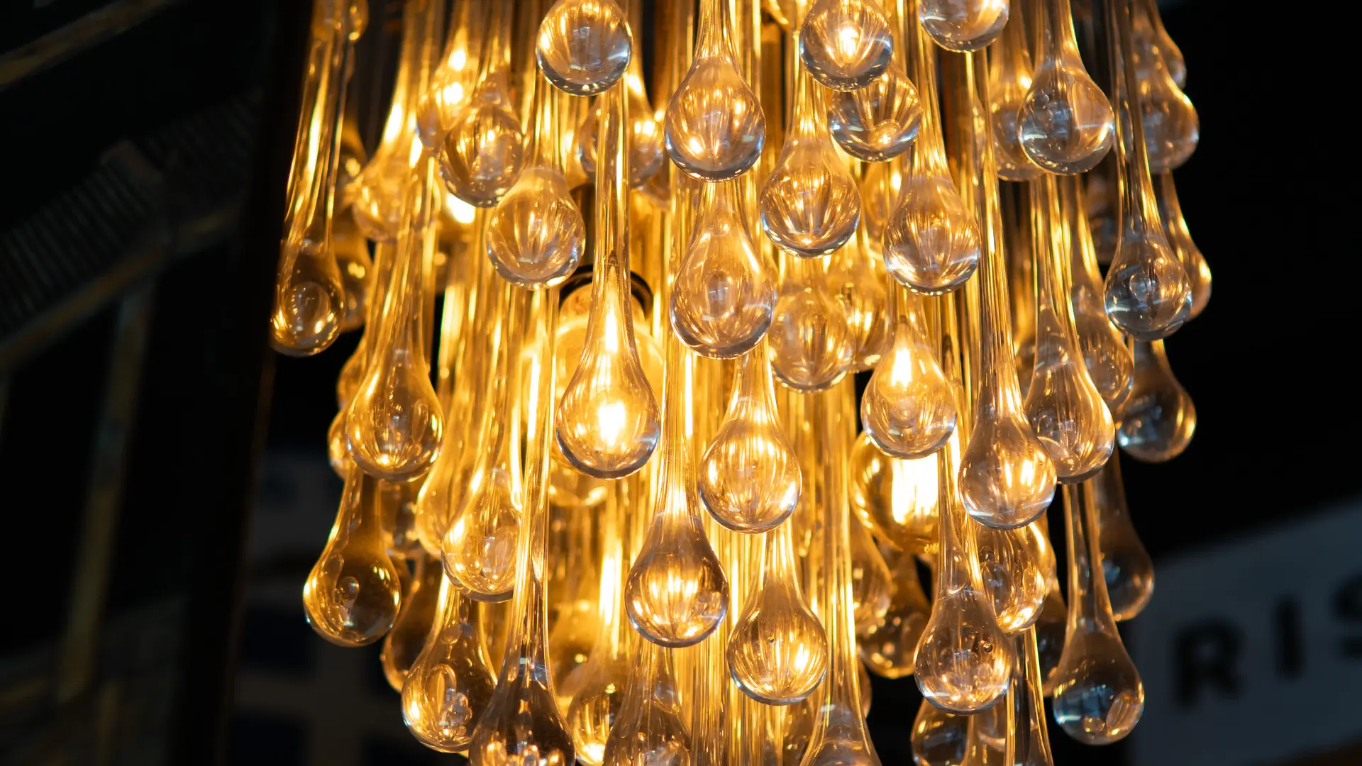 Un lustre scintillant compose une chute de gouttes de verre dorées offrant une lumière chaude et hypnotique.