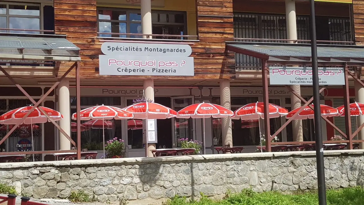 Restaurant frontage in summer with outdoor terrace furnished with tables, chairs, and red parasols. Sign with the inscription: Pourquoi pas ? Crêperie Pizza Mountain specialties
