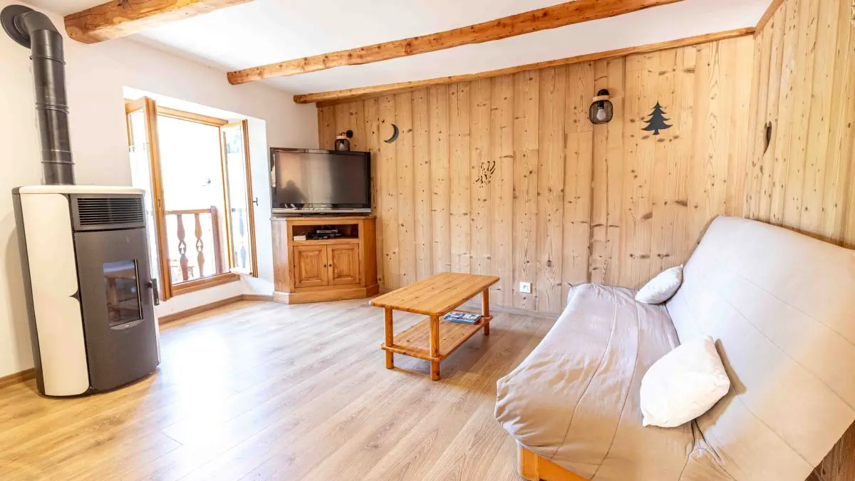 Séjour moderne et lumineux avec canapé, table basse, TV, poêle à bois, porte-fenêtre, ameublement bois et parquet au sol
