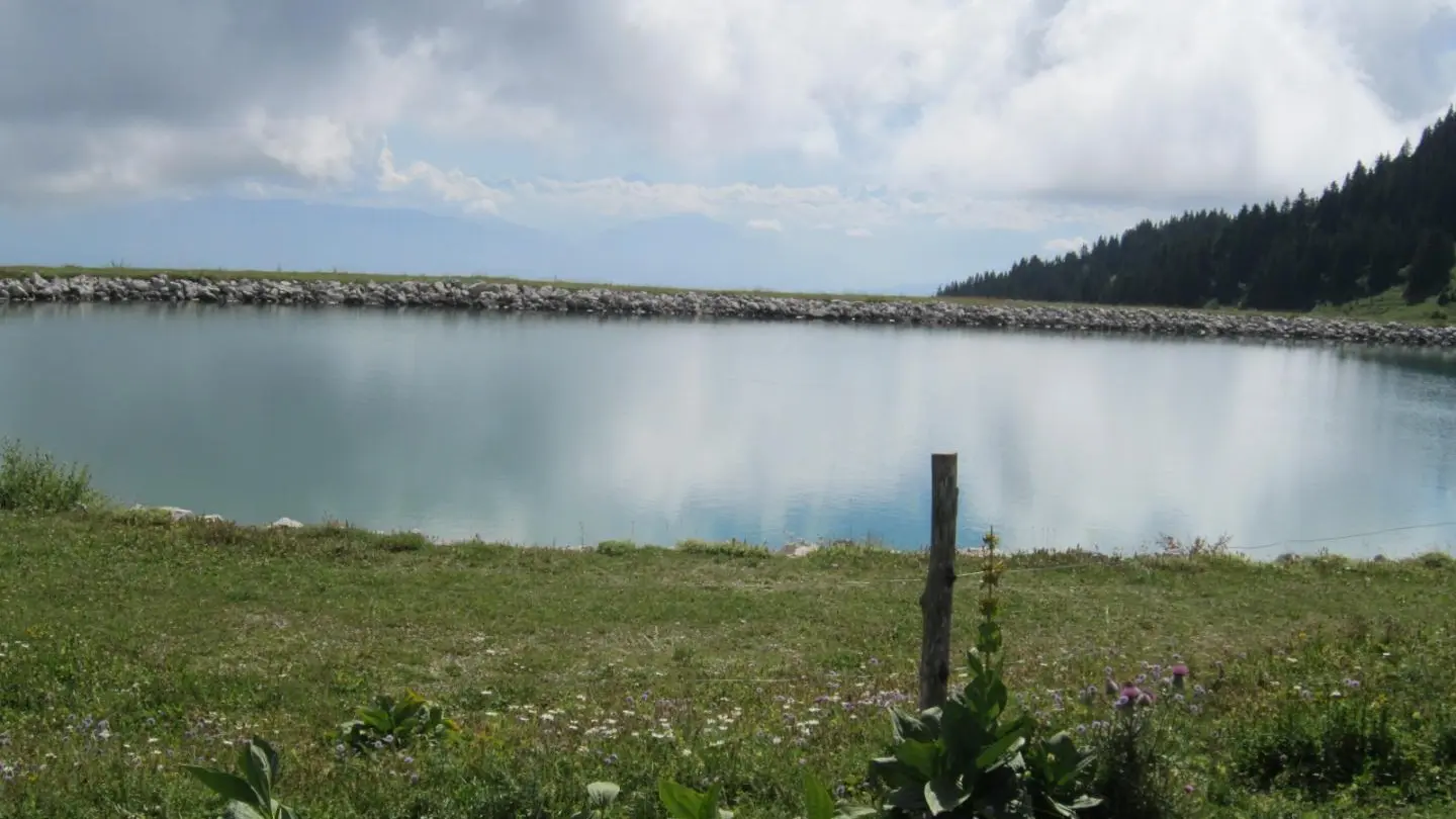 en haut des pistes,lac artificiel pour neige de culture et chaine du Mont Blanc derrière les nuages.