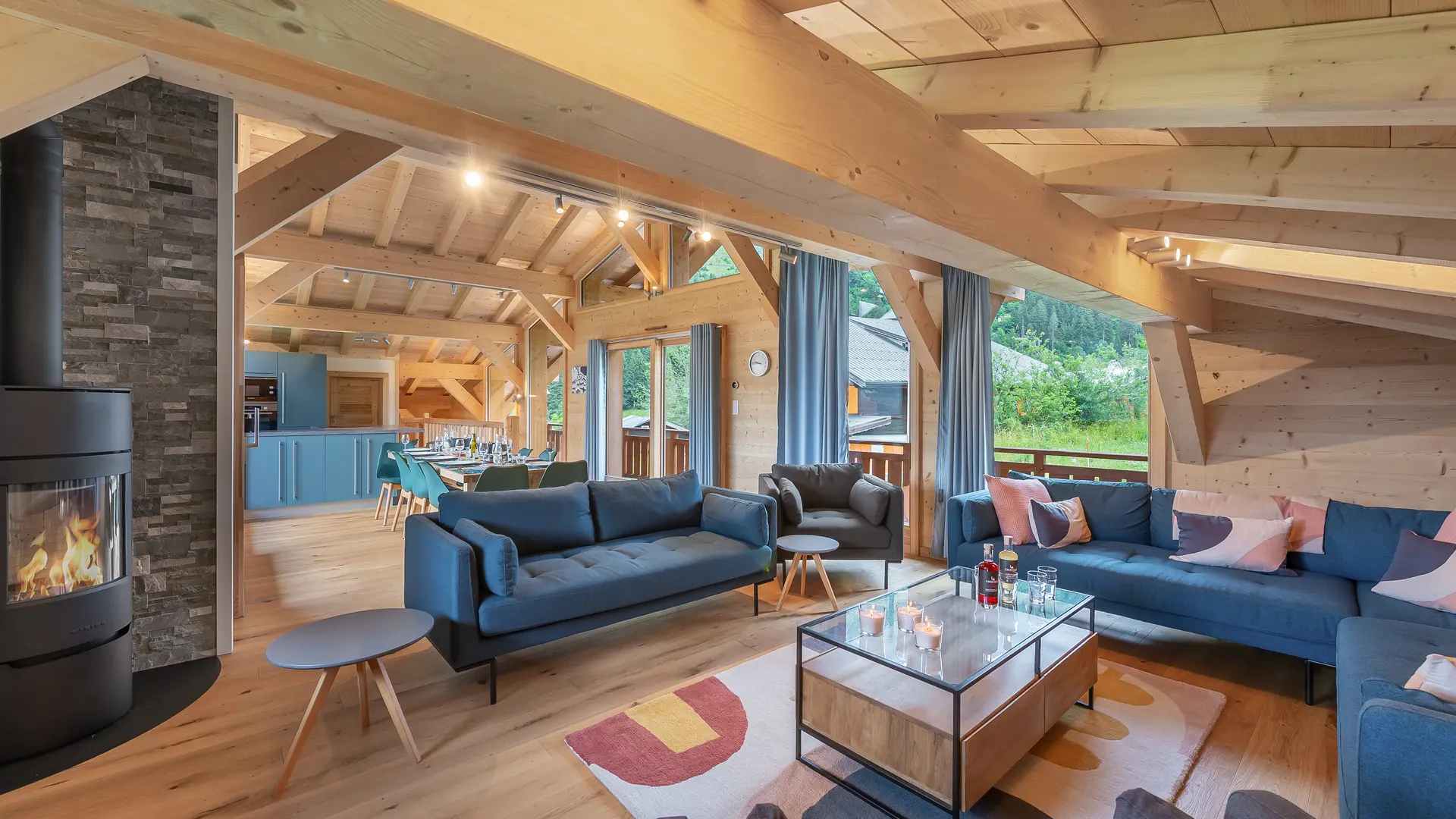 Grand salon lumineux avec canapés et fauteuils, poele à bois, poutres apparentes