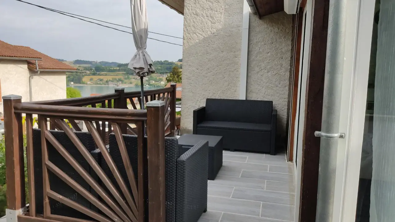 Une terrasse avec deux canapés d'extérieur et une table basse assortie en osier d'ombre permet de profiter d'une vue sur les eaux du lac et sa colline au dernier plan