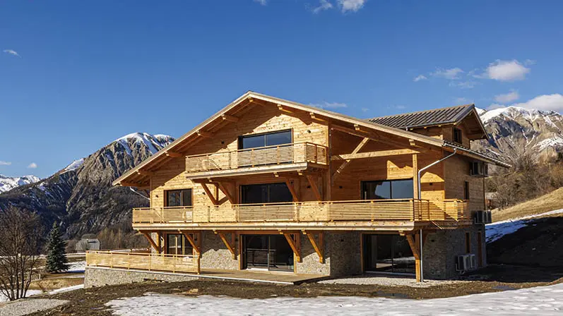 Large isolated three-storey chalet made of wood and stone,  large wooden terraces and french windows, mountain scenery