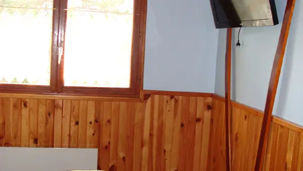 Vue sur un coin de chambre à coucher lumineuse, ameublement en bois, lambris, lit double, TV et fenêtre