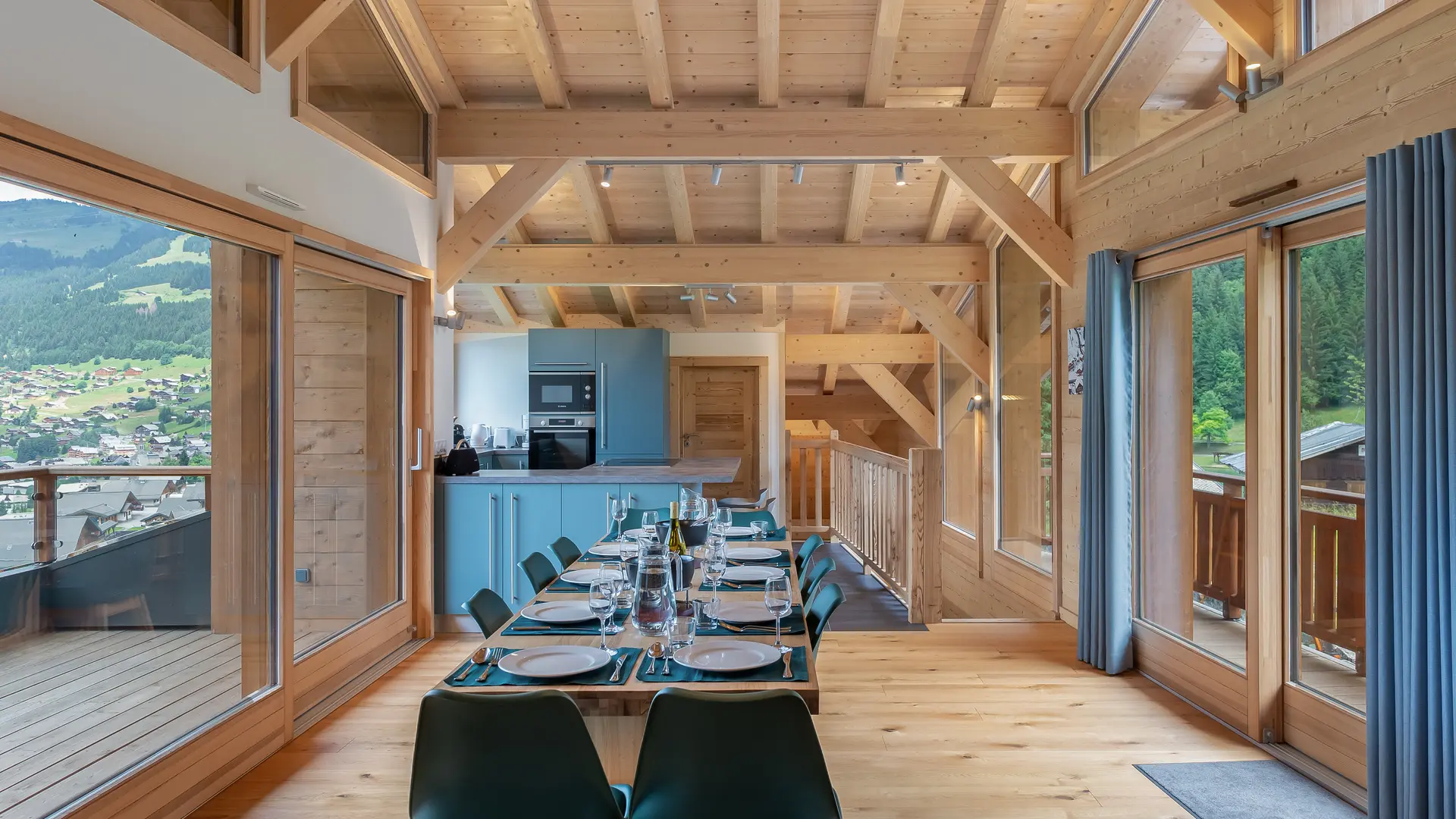 Espace salle à manger avec grande table, fenêtres des deux côtés, cuisine en arrière plan