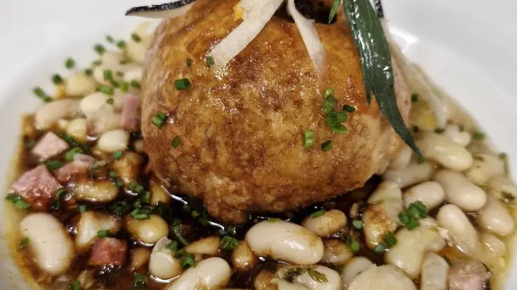 La tourte au foie gras du chef déposé sur des haricots mogettes dans une assiette blanche.