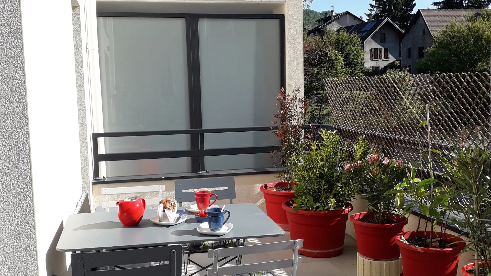 La terrasse est aménagée avec un salon de jardin et des jardinières colorées.