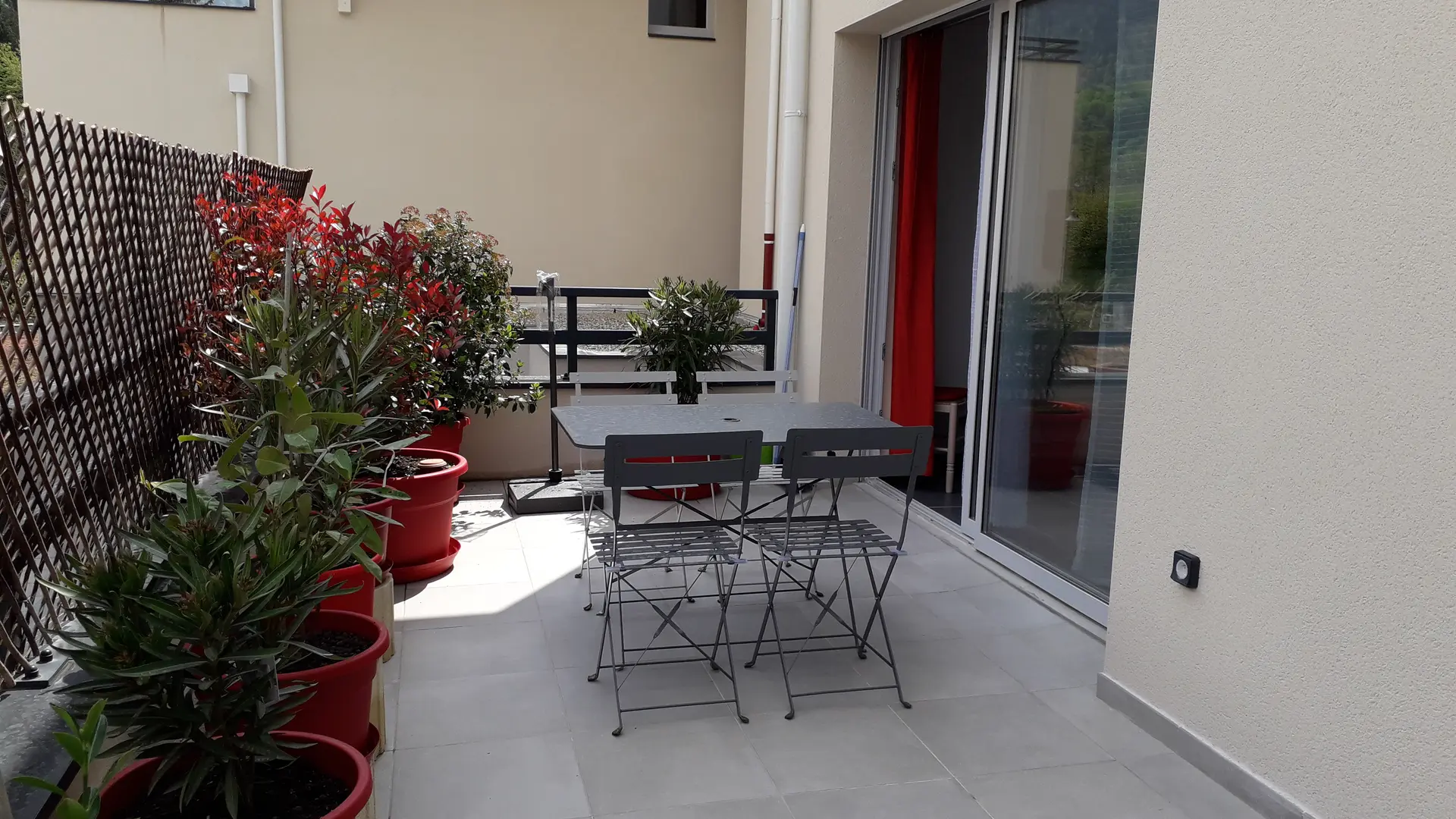 Cette terrasse extérieure est accessible par une porte coulissante. Elle est aménagée avec un salon de jardin en métal et des plantes en pots.