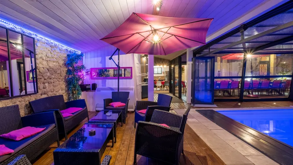 Sous la véranda ouverte de nuit, éclairée, avec salon de jardin.