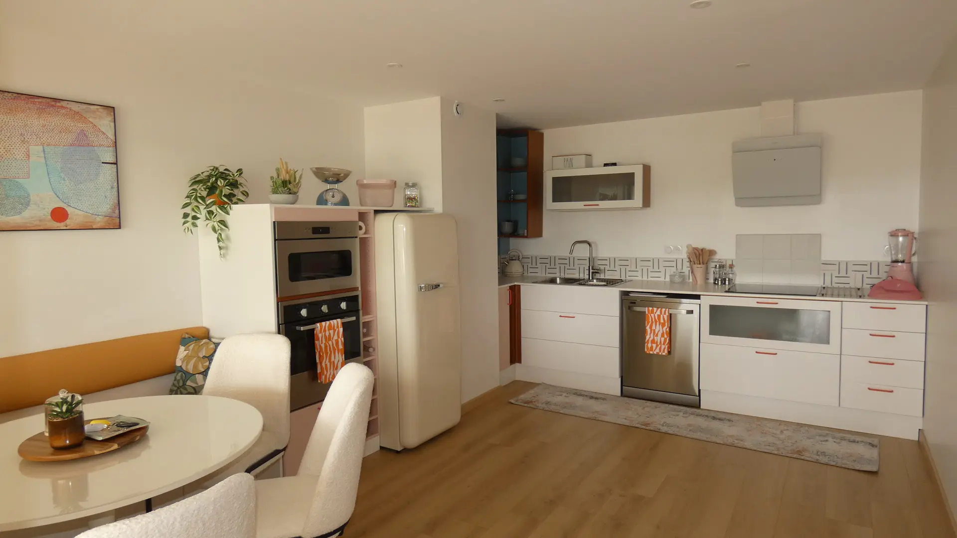 Vue sur une spacieuse et lumineuse cuisinie entièrement équipée. Décorée dans des teintes poudrées roses ou beiges, elle est possède également une table à manger avec ses chaises et une banquette.