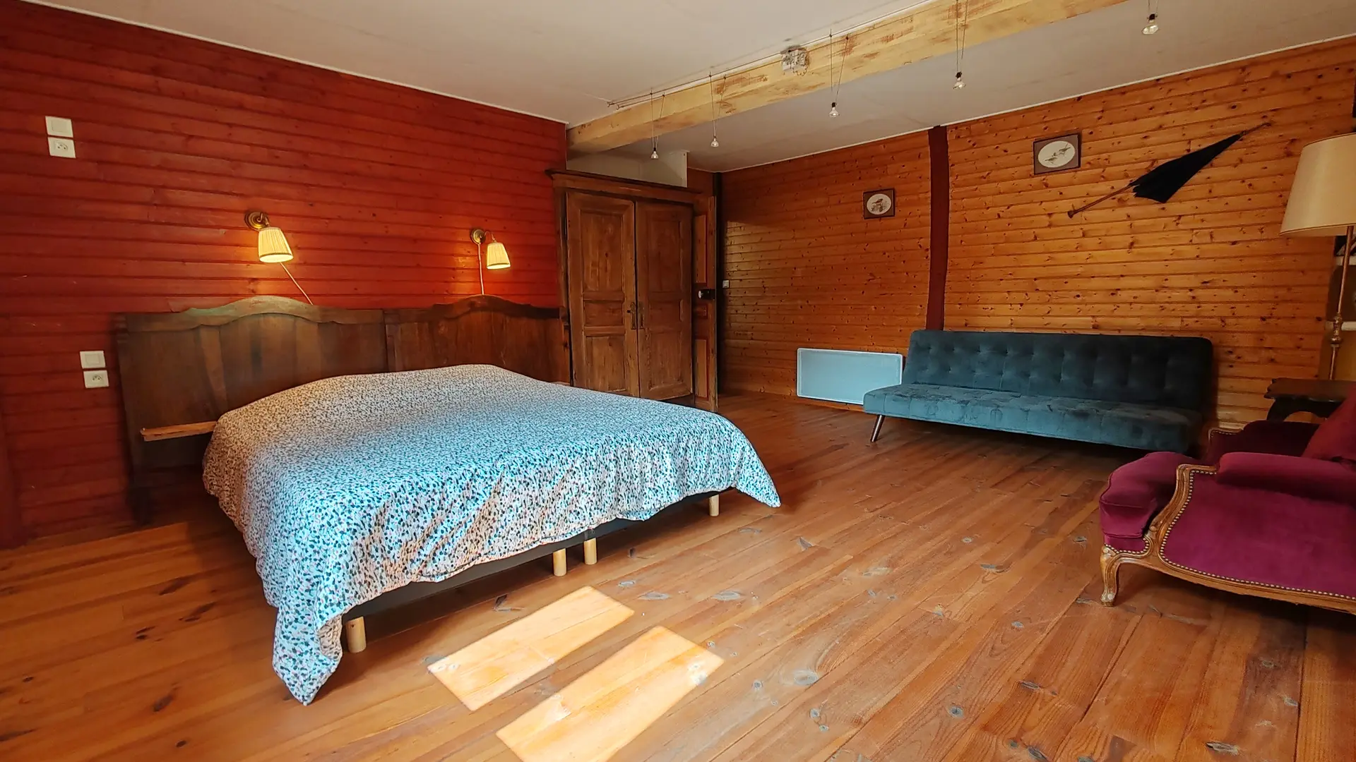 On se trouve dans une chambre spacieuse aux couleurs chaudes de l'automne dont le bois est la matière de décoration ( murs et sol). On voit un lit pour deux personnes avec deux luminaires au-dessus de la tête de lit. Un grand placard à l'ancienne permet de ranger ses affaires. La pièce comporte aussi un canapé velours bleu et deux fauteuils velours violine. La décoration est complété par deux tableaux un vieux parapluie et un lampadaire de salon permettant de s'adonner à la lecture dans le calme et la quiétude du lieu.