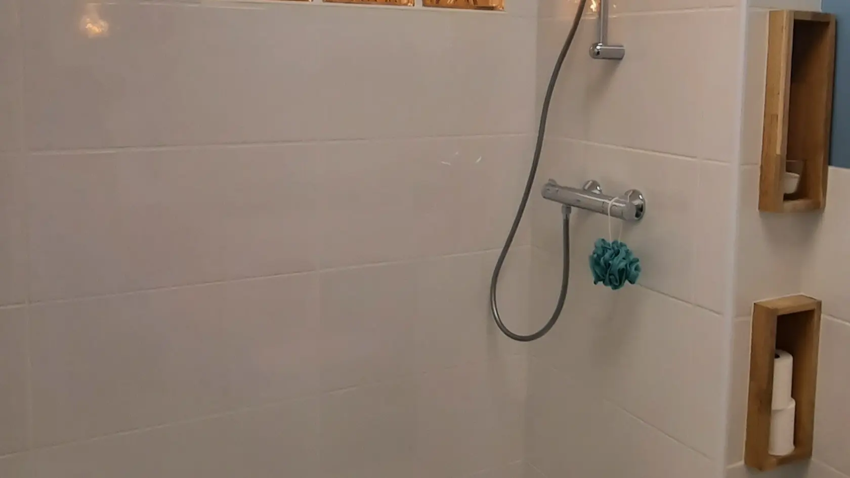 Cette salle d'eau est équipée d'une douche avec un receveur extra-plat. Un pommeau de douche est fixé au mur. Une petite fenêtre laisse entrer la lumière naturelle.