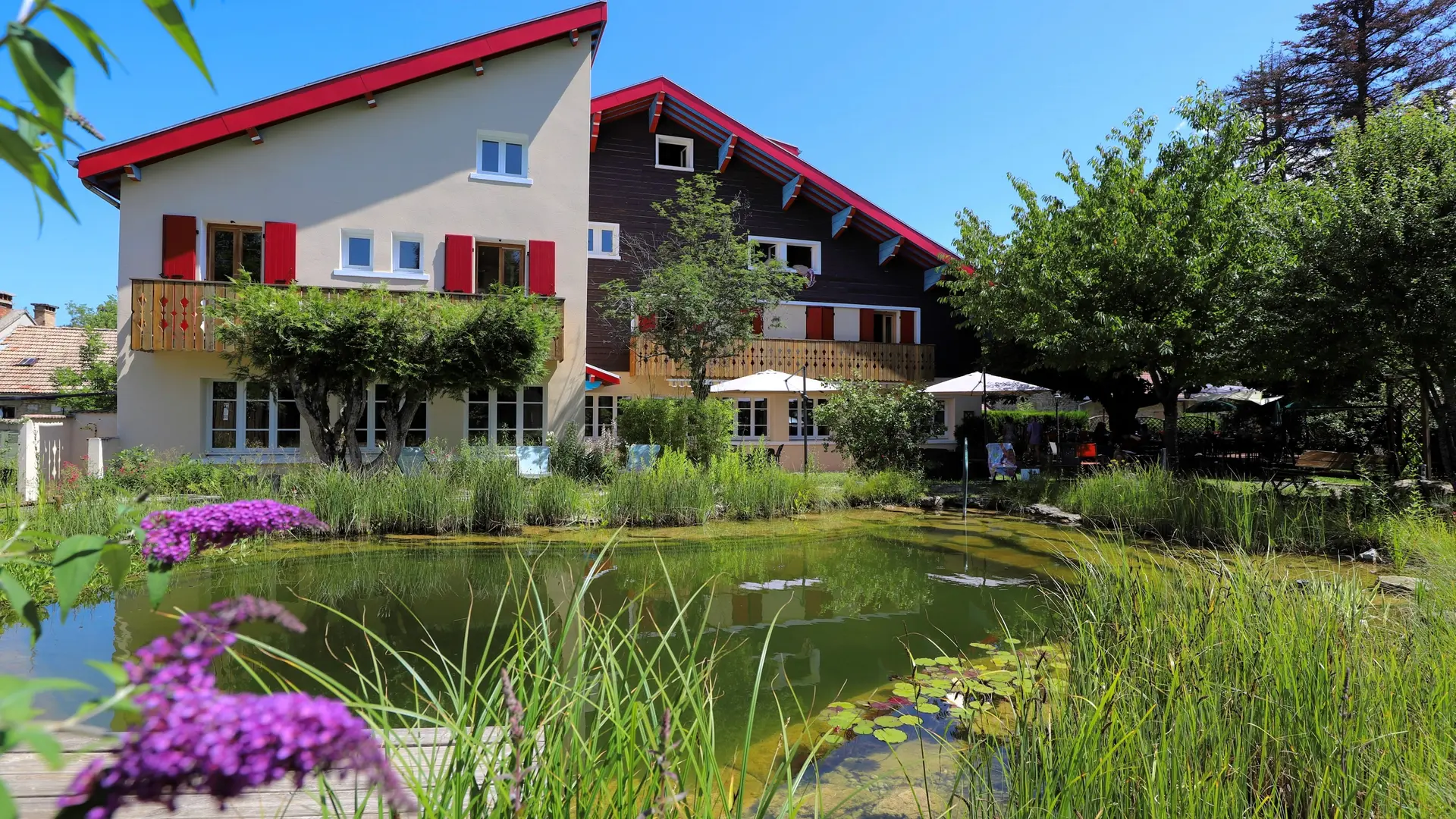 Vue extérieure de l’établissement regroupant l’hôtel et le restaurant avec une mare naturelle au premier plan