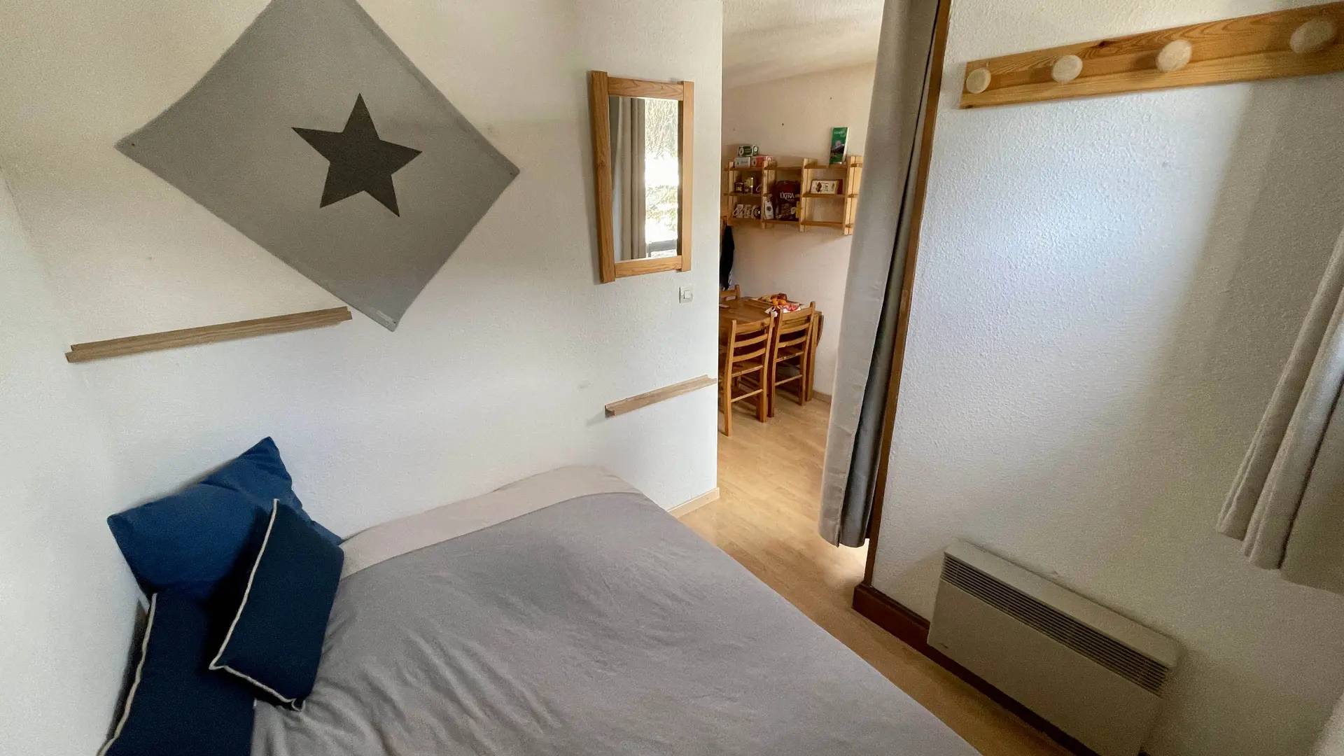 Coin nuit avec lit double, miroir, radiateur et patère, fermeture de la pièce par un rideau