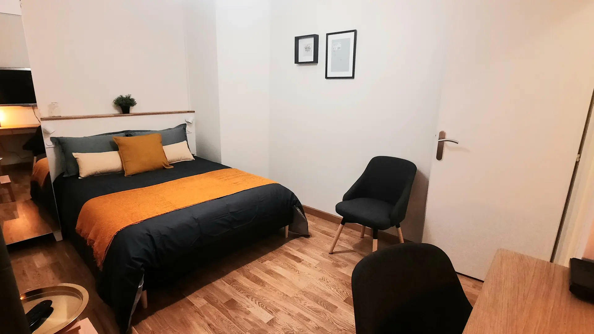 Cette chambre est aménagée avec un lit double recouvert d'une couette aux couleurs vives. Un bureau avec une chaise est placé près de la fenêtre. Une armoire de rangement est située contre le mur opposé au lit.