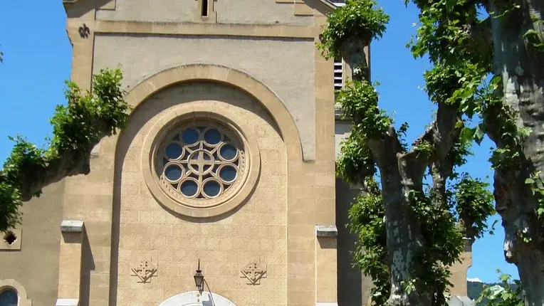 Église en pierre marron avec un grand vitrail rond au dessus de l'entrée.